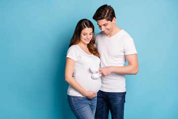 Photo of positive spouse look belly finger baby booties steps playing isolated on blue color background