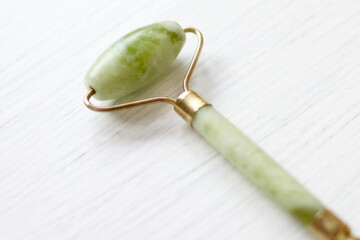 Green jade face roller, natural stone for skin care, on white backdrop. Tool for facial lifting...