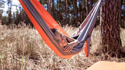 Cute girl having rest in hammock in the wild forest during local vacation, family summer weekend,...