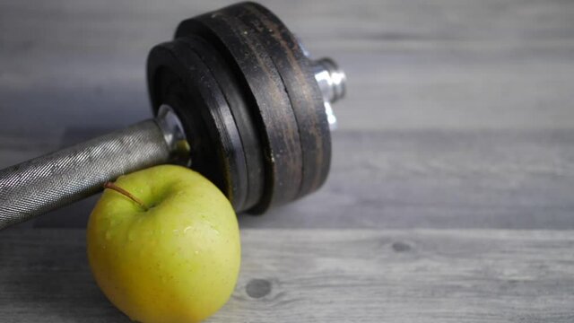 Close-up of green apple and dumbbell on wooden floor