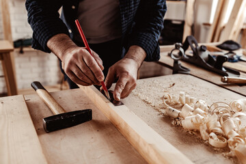 Carpenter makes pencil marks on a wood plank