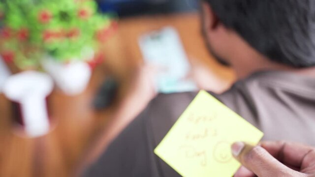 Pasting aprils fools day sticker on young mans shoulder while busy on mobile phone - concept of April fool day celebration and making fool