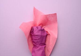female hand in a pink rubber glove holds a pink cleaning rag on a purple background