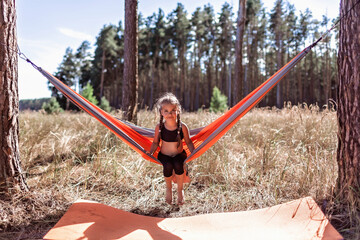 Cute girl having rest in hammock in the wild forest during local vacation, family summer weekend, social distance, unity with nature, digital detox, active lifestyle