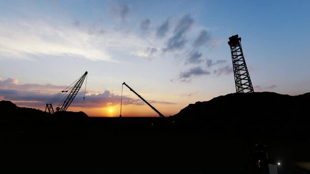Moving silhouettes of cranes on a construction site, sunset time
