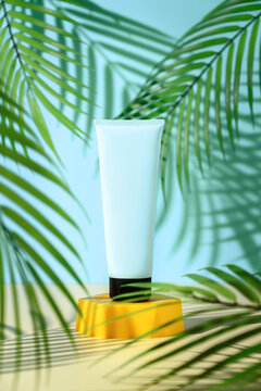 Ad template for sunscreen tube mock-up displayed on yellow podium on surrounded by palm leaves. Blue background, vertical orientation