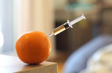 Close up of a vaccine syringe sticking in an orange on a table.
