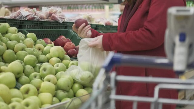 Girl in grocery store buys apples. She put the fruit in a bag. In the foreground is a cart with a validator for reading the barcode. Concept of healthy nutrition and vitamin intake