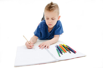 Young boy lying on floor with pencils on a sketch book with a look of concentration, close up view....