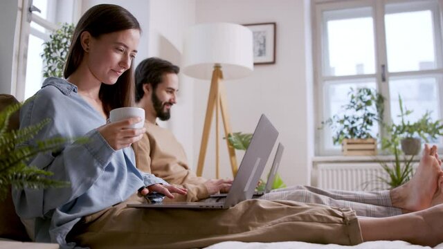 Side view of couple using laptops on bed indoors, home office concept.