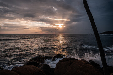 Skaliste wybrzeże na tle wzburzonego oceanu z falami i zachodzącego słońca. © insomniafoto