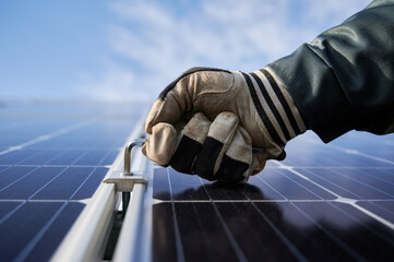 Close up of worker hand in glove holding a hex key, installing photovoltaic solar panel with blue...