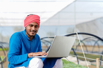 Young indian farmer using laptop at greenhouse or poly house