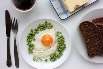 Fried egg with green peas, rye bread, butter and cup of black herbal tea on white table background. Healthy breakfast or brunch concept. Top view. Flat lay food
