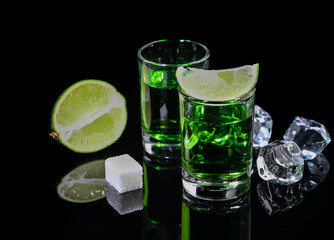 Absinthe shots with lime slices and sugar on black background