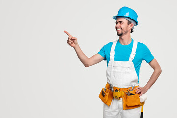 Cheerful handyman with professional tools pointing at blank space