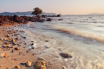 Beautiful sunset seascape with rock on sand beach.
