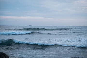 Obraz premium Surfer na fali, na tle oceanu, skał i wzburzonej wody.
