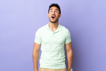 Young handsome man isolated on purple background looking up and with surprised expression