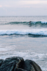 Surfer na fali, na tle oceanu, skał i wzburzonej wody. © insomniafoto