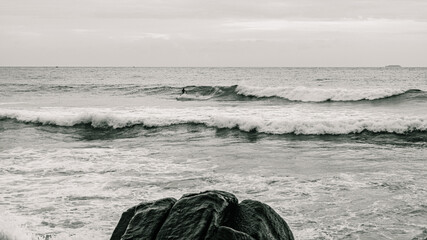 Surfer na fali, na tle oceanu, skał i wzburzonej wody. © insomniafoto