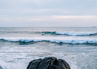 Surfer na fali, na tle oceanu, skał i wzburzonej wody. © insomniafoto