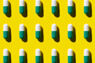 White and green pill capsule pattern on a yellow background. Hard shadows.