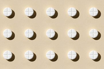 Round tablet pill pattern on a beige background. Hard shadows.