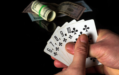 Crossed fingers bring good luck. Poker cards with a straight flush combination. Close-up of a gambler hand is holding playing cards in casino