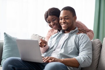 Closeup of cheerful black couple using laptop together at home