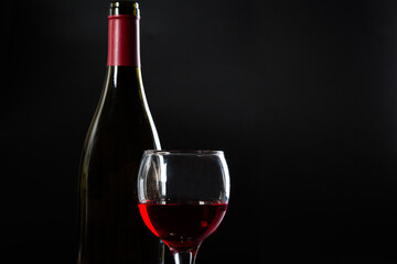 Wine bottle and glass with red wine on dark glossy background.