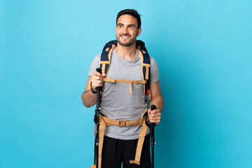 Young caucasian man with backpack and trekking poles isolated on blue background thinking an idea...