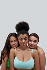 Portrait of three diverse young women wearing colorful underwear looking at camera, posing together over light background
