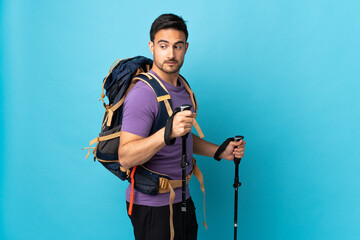Young caucasian man with backpack and trekking poles isolated on blue background . Portrait
