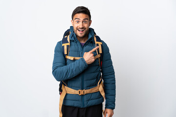 Young mountaineer man with a big backpack isolated on white background pointing finger to the side
