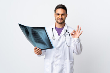 Young doctor man holding a radiography isolated on white background showing an ok sign with fingers