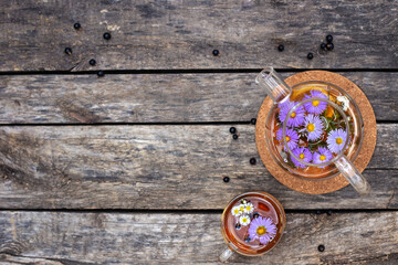 Fototapeta na wymiar Herbal tea in glass teapot and cup on cork coaster with violet flowers and black current on wooden background with copy space. Healthy summer drink.