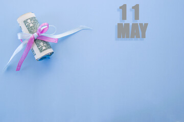 calendar date on blue background with rolled up dollar bills pinned by blue and pink ribbon with copy space. May 11 is the eleventh  day of the month
