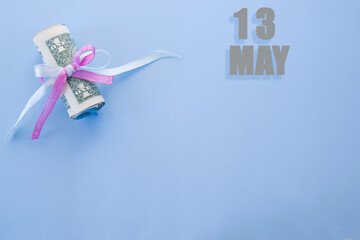 calendar date on blue background with rolled up dollar bills pinned by blue and pink ribbon with copy space. May 13 is the thirteenth day of the month