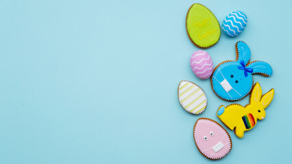 Pandemic banner. Happy Easter. Quarantine holiday celebration. Colorful gingerbread bunny cookie in protective face mask painted egg set with minimal design isolated on blue copy space background.