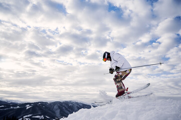 Naklejka na ściany i meble Side view of male skier in winter jacket sliding down snow-covered slopes on skis under beautiful cloudy sky. Man freerider in helmet skiing on fresh powder snow in winter high mountains.