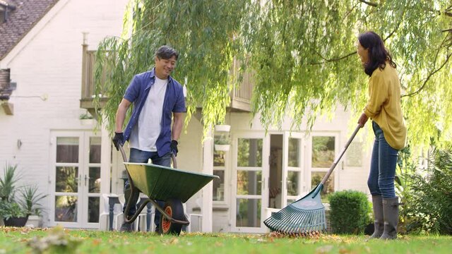 Mature Asian couple working in garden at home raking leaves into barrow- shot in slow motion