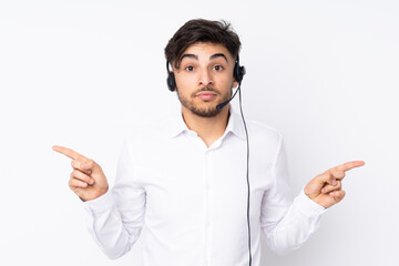 Telemarketer Arabian man working with a headset isolated on white background pointing to the laterals having doubts