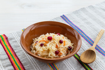 Pickled cabbage with cranberries in a clay bowl on a towel.