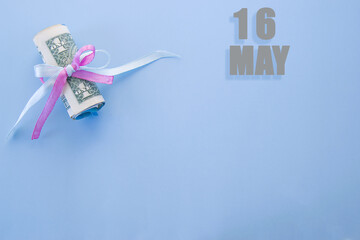 calendar date on blue background with rolled up dollar bills pinned by blue and pink ribbon with copy space. May 16 is the sixteenth day of the month