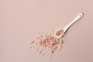White ceramic spoon and scattered pink himalayan salt on a powder pink background. Copy space, top view. Healthy cooking, home care concept. Selective focus. - obrazy, fototapety, plakaty