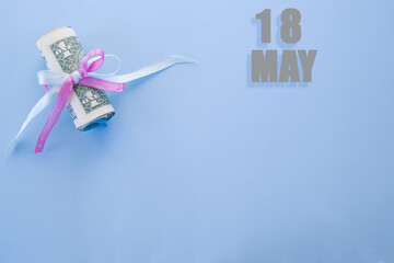 calendar date on blue background with rolled up dollar bills pinned by blue and pink ribbon with copy space. May 18 is the eighteenth day of the month