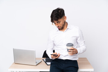 Arabian man in a office isolated on white background holding coffee to take away and a mobile