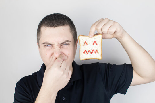 Conceptually about gluten intolerance. The man holds in his hand a piece of bread on which an angry expression is painted. Celiac disease, fear of cereals, manifestation of allergies
