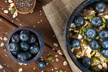 Blueberries in a ceramic bowl with wooden spoon of chia seeds and bowl of oatmeal porridge on a wooden background. Top view.